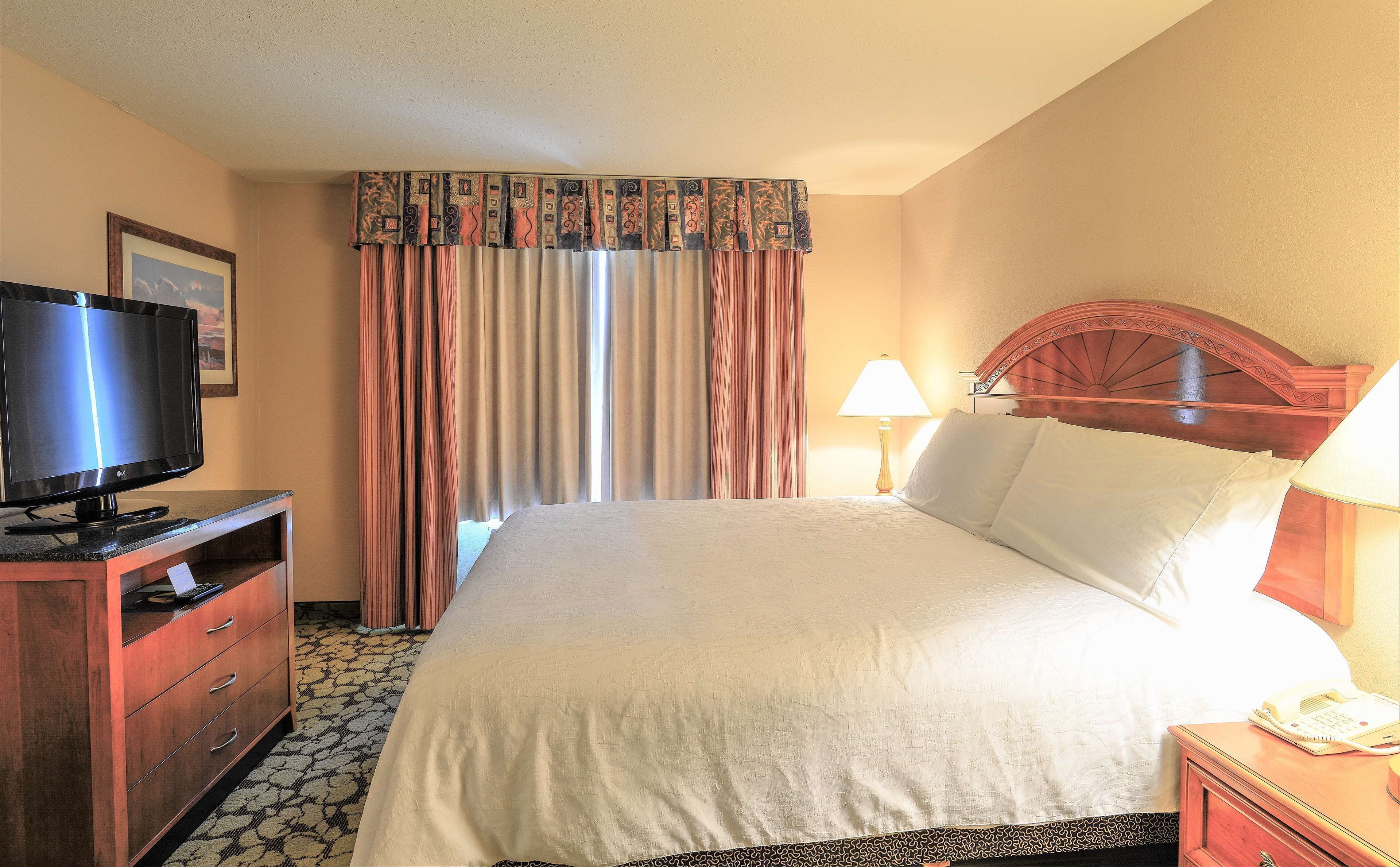A hotel room with a bed, a TV, a desk with drawers, a lamp, and a telephone.