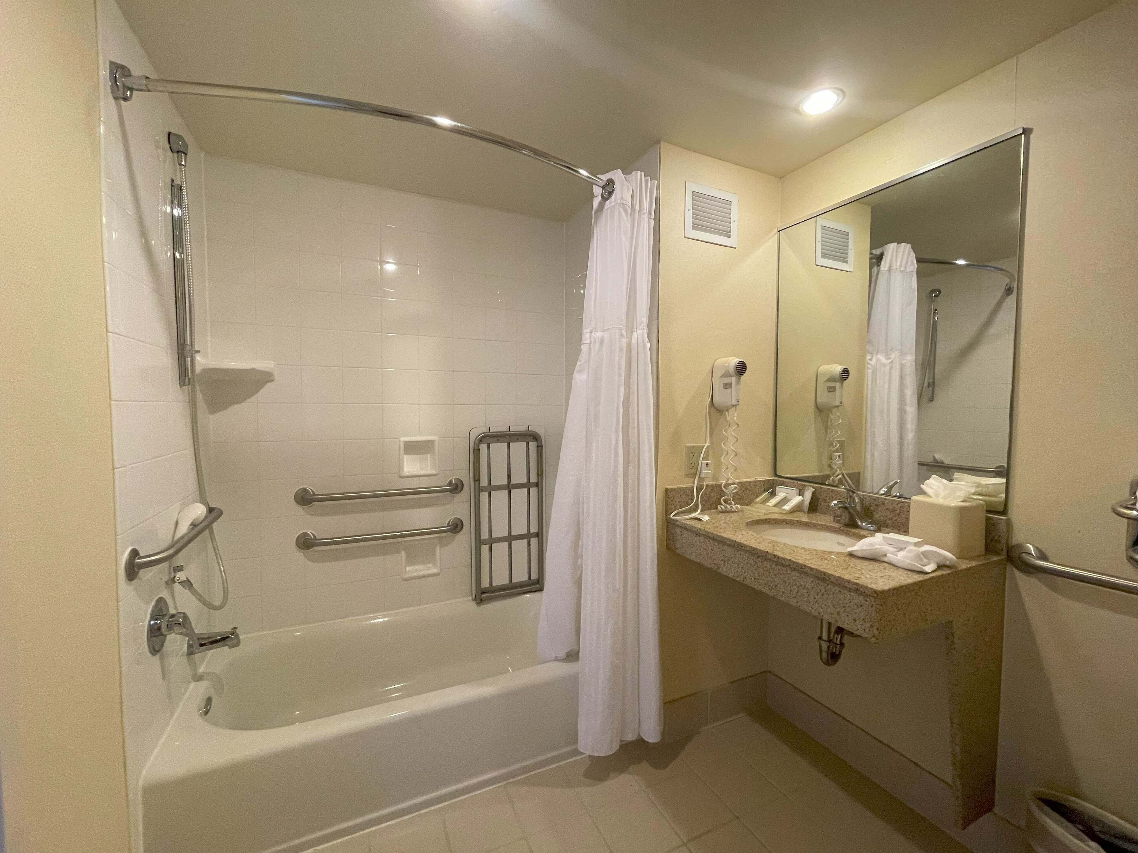 Un baño con bañera, ducha, tocador con espejo y perchero para toallas.