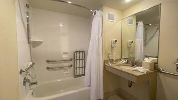 Un baño con bañera, ducha, tocador con espejo y perchero para toallas.