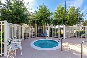 A swimming pool with a white fence, lounge chairs, and a hot tub.