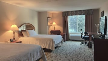 A hotel room with two beds, a desk with a computer, a chair, and a window with curtains.