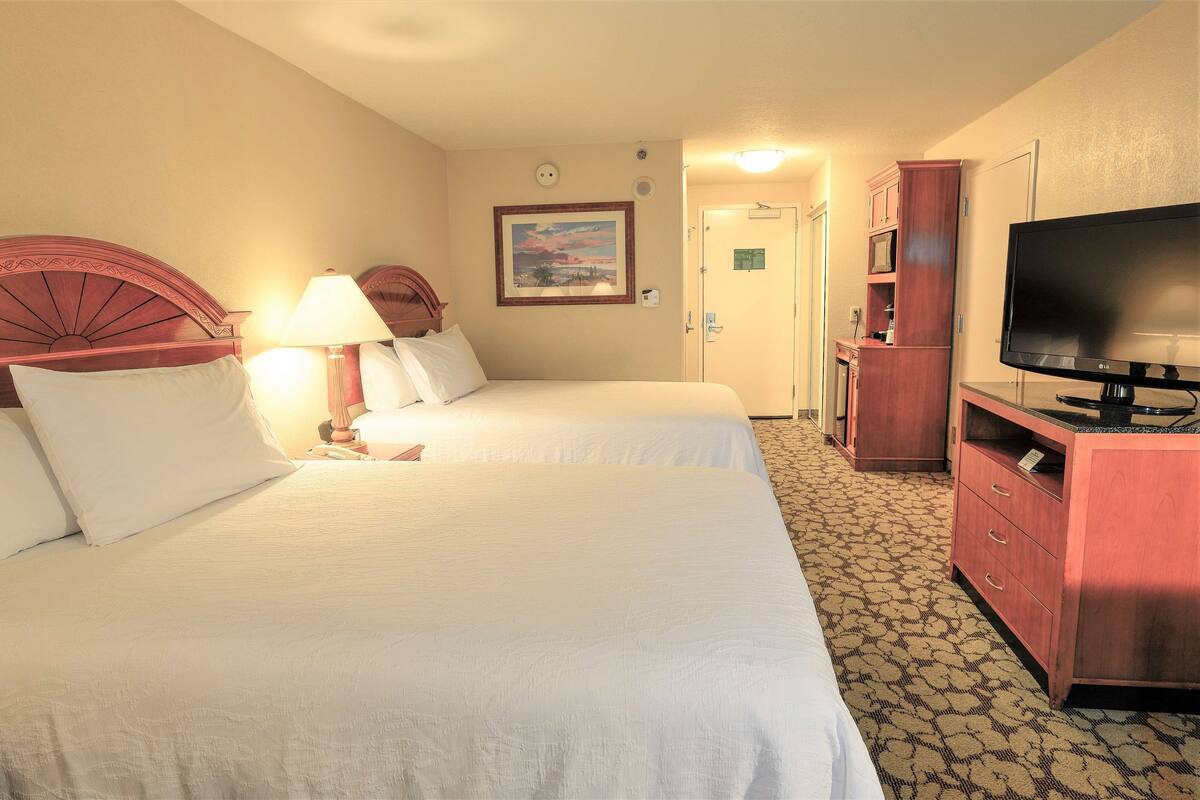 Quarto de hotel com duas camas, televisão, escrivaninha e armário.