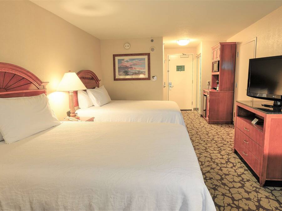 A hotel room with two beds, a television, a desk, and a cabinet.
