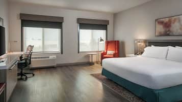 A hotel room with a bed, desk, chair, and a large window.