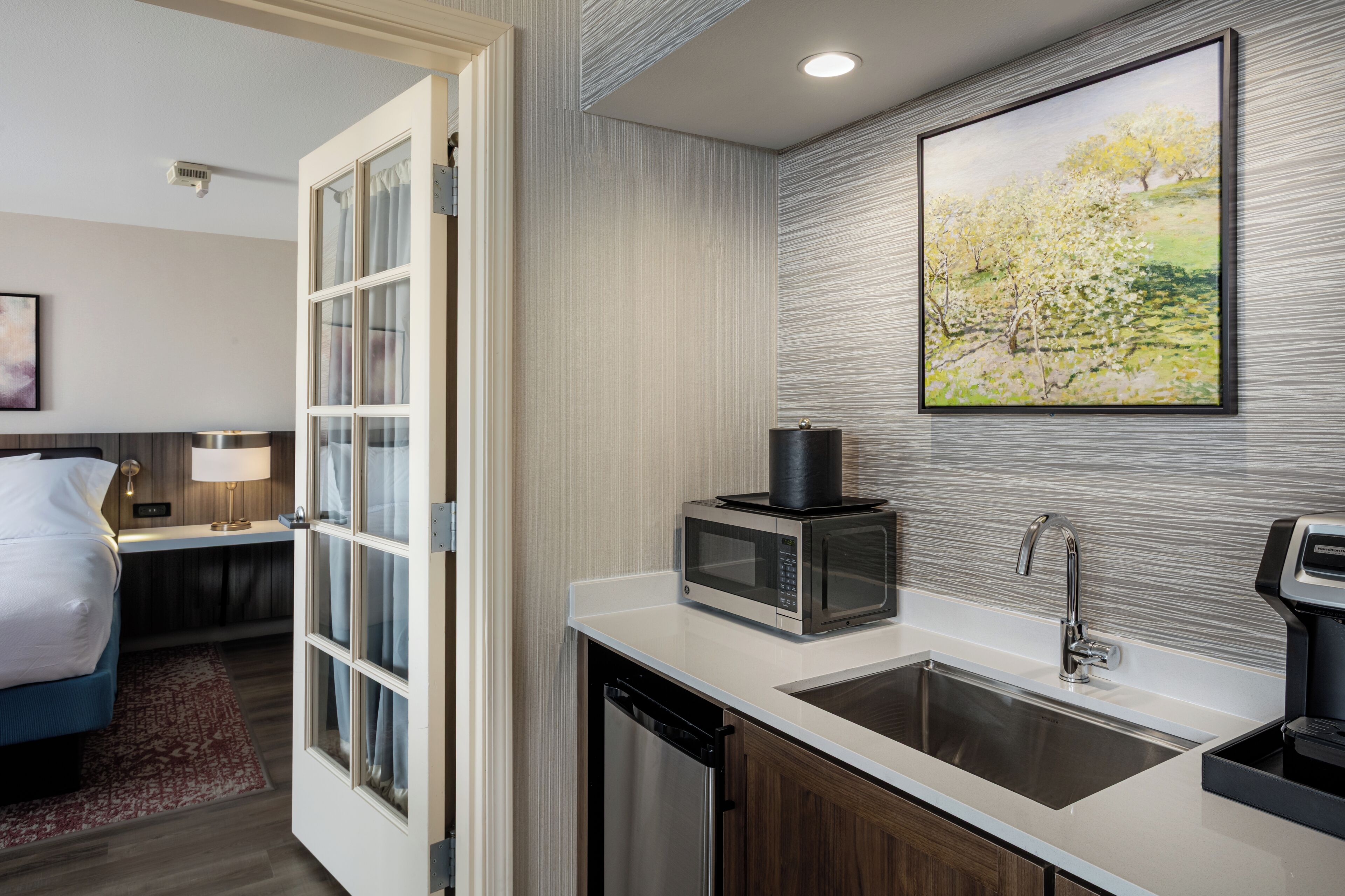 A modern kitchen with a microwave, sink, and a painting on the wall.