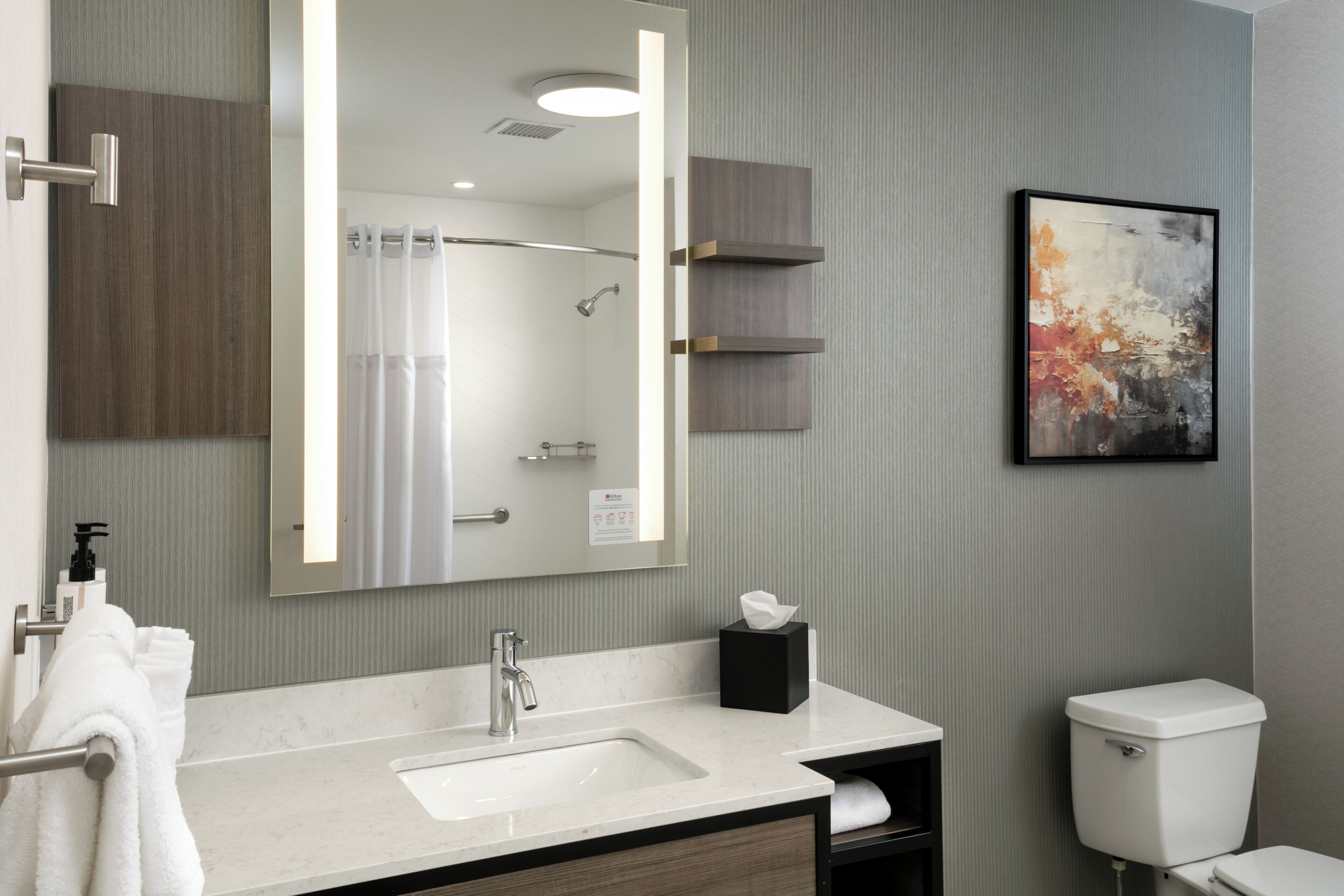 A modern bathroom with a large mirror, a sink, a toilet, and a towel rack.
