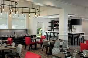 Un interior de restaurante moderno con barra, mesas y una pantalla de televisión.