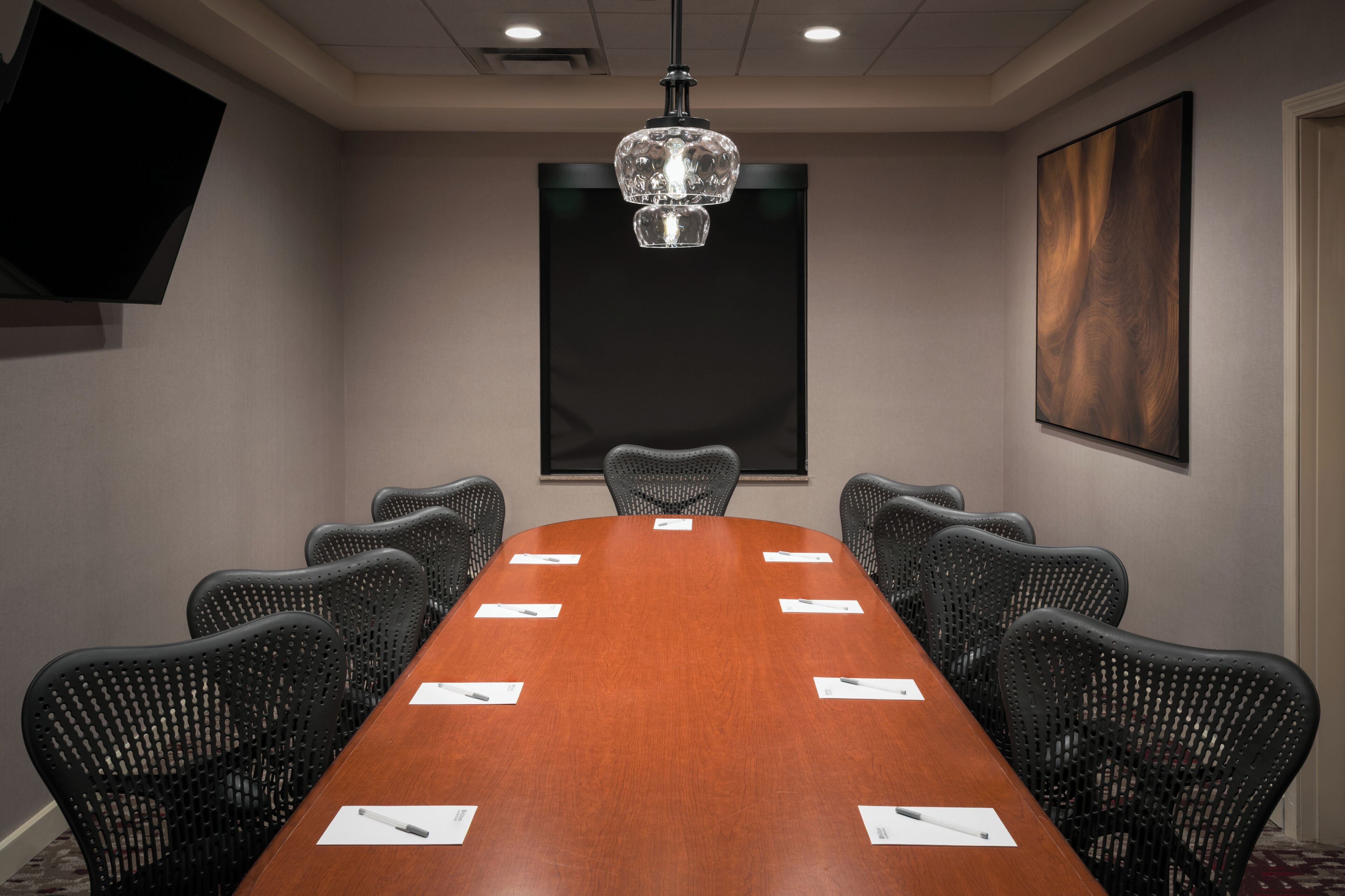 A conference room with a long table, black chairs, a chandelier, a flat-screen TV, and a large abstract painting on the wall.