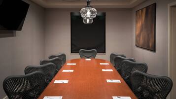 A conference room with a long table, black chairs, a chandelier, a flat-screen TV, and a large abstract painting on the wall.
