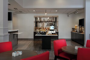 A modern hotel kitchen with a central island, stainless steel appliances, and a seating area with red chairs. - Hilton Garden Inn Tri-Cities/Kennewick (Kennewick)