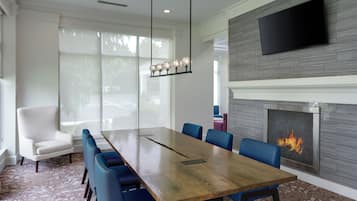 A conference room with a long wooden table, blue chairs, a white armchair, a fireplace, and a flat-screen TV mounted on the wall.