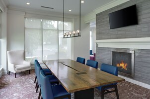 A conference room with a long wooden table, blue chairs, a white armchair, a fireplace, and a flat-screen TV mounted on the wall.