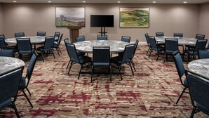 A conference room with multiple tables and chairs, a flat-screen TV, and two landscape paintings on the walls.