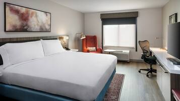 A hotel room with a large bed, a desk with a chair, a TV, and a window with blinds.