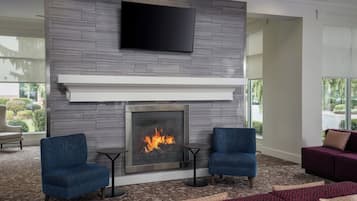 A modern living room with a fireplace, two blue armchairs, a red sofa, and a flat-screen TV mounted on the wall.