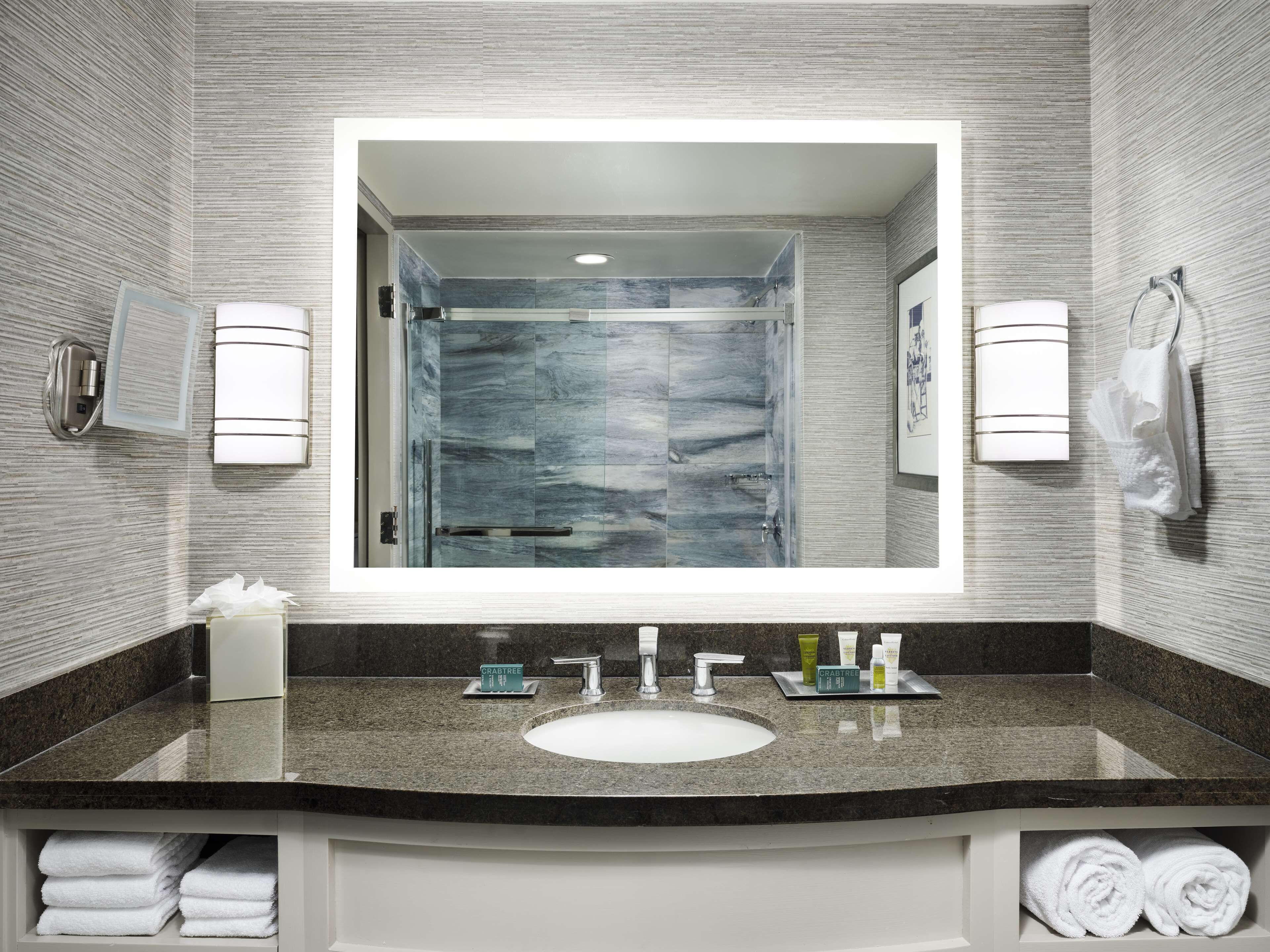 Une salle de bain moderne avec un grand miroir, un comptoir en granit et une cabine de douche en verre.