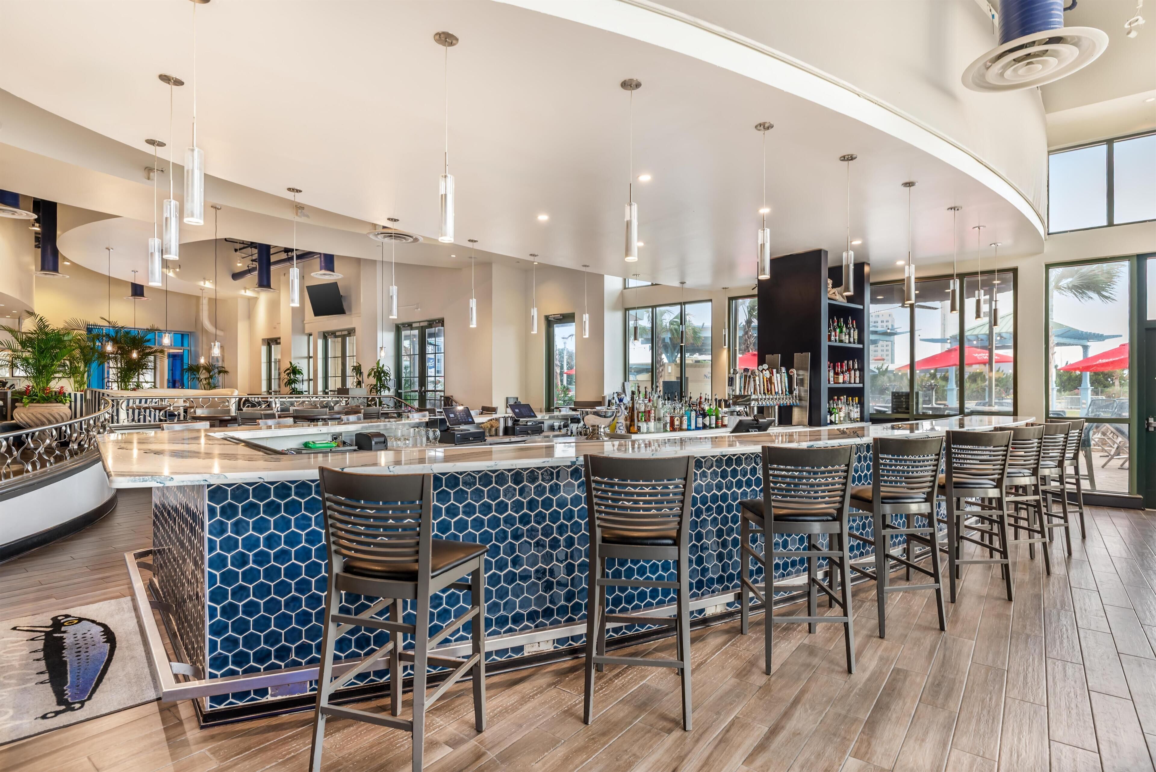 Uma área de bar com balcão curvo, banquetas e vista para o exterior.