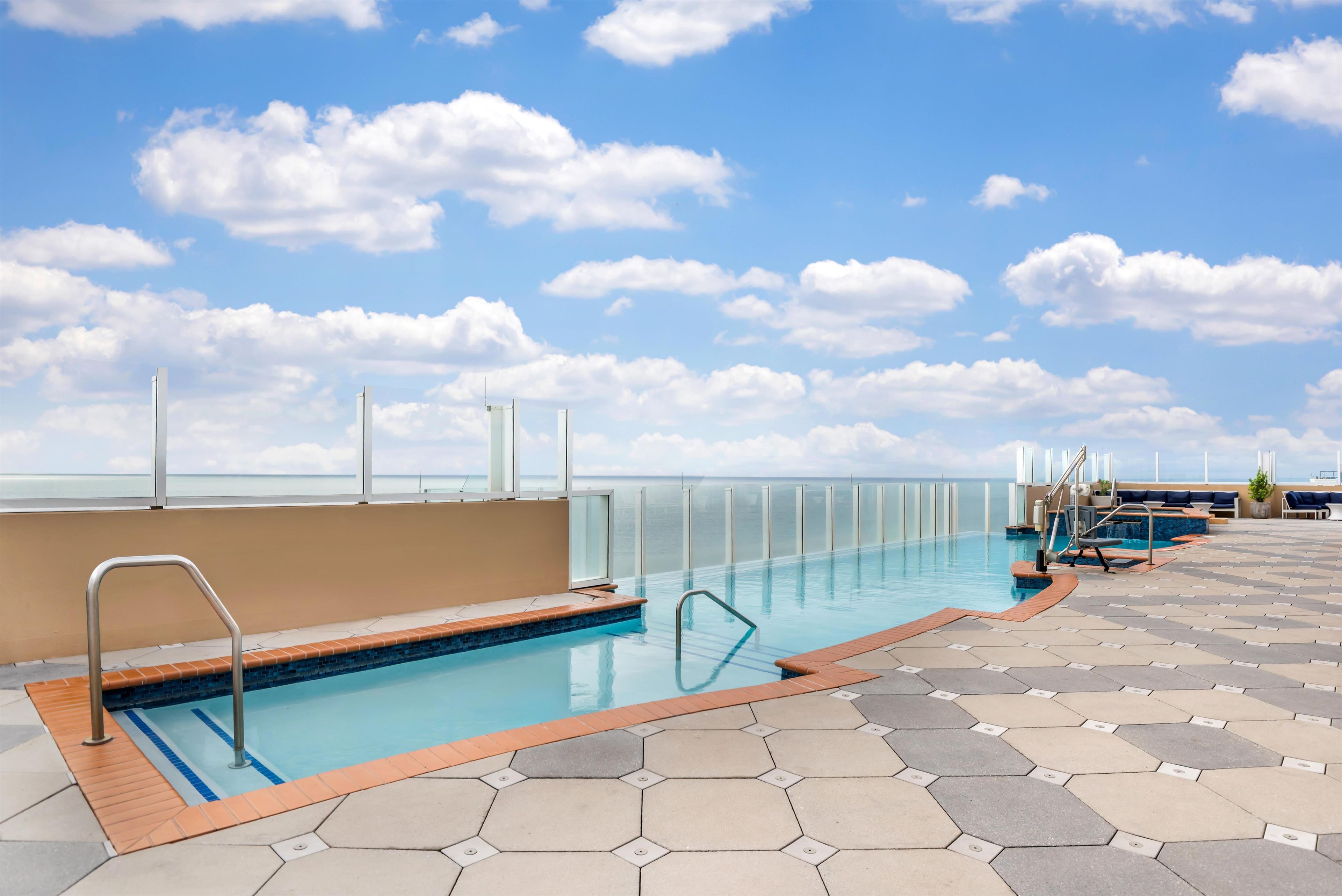 A pool area with a clear view of the ocean, a tiled deck, and a lounge area with seating.