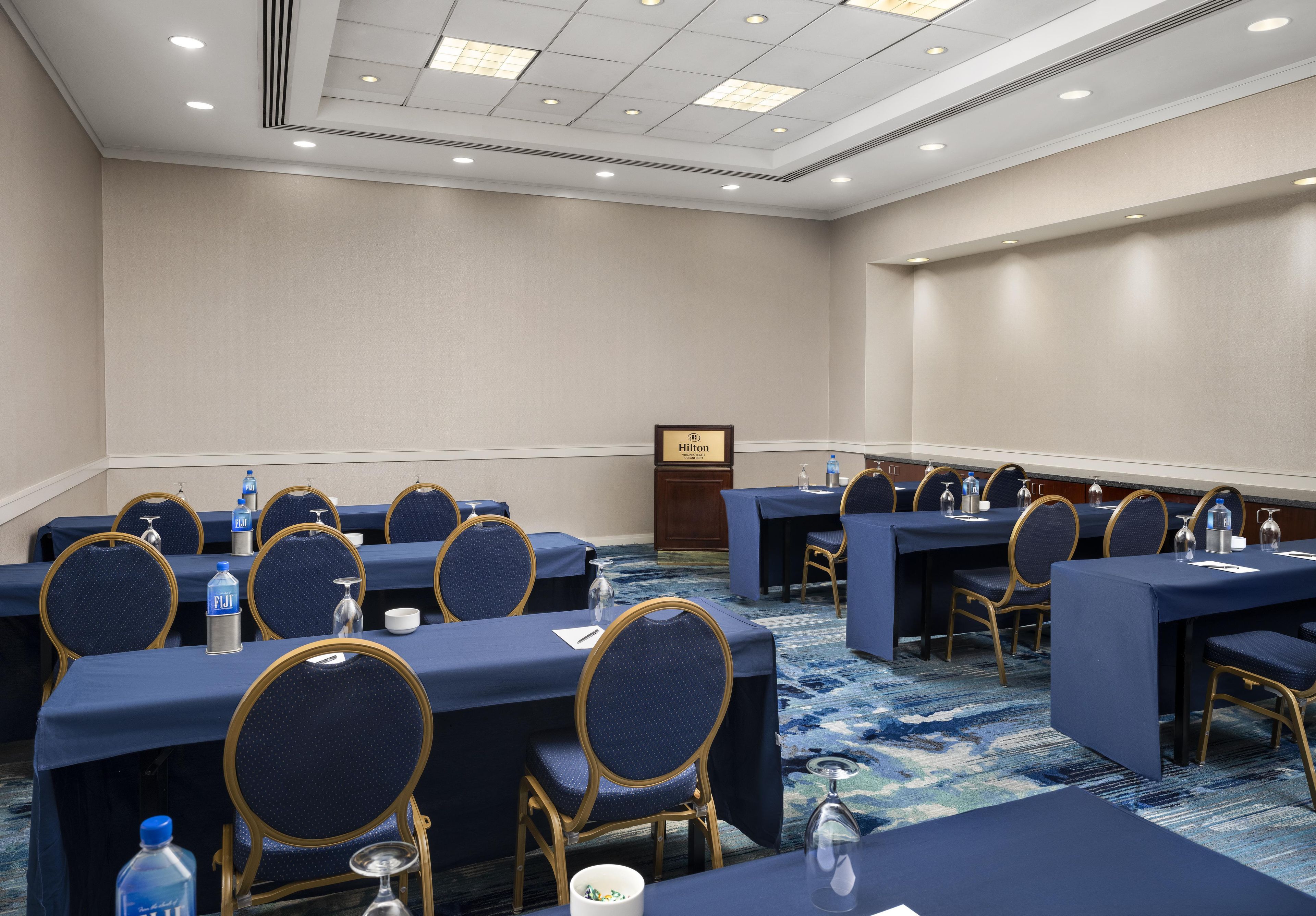 A conference room with multiple tables and chairs, a podium, and a water dispenser.