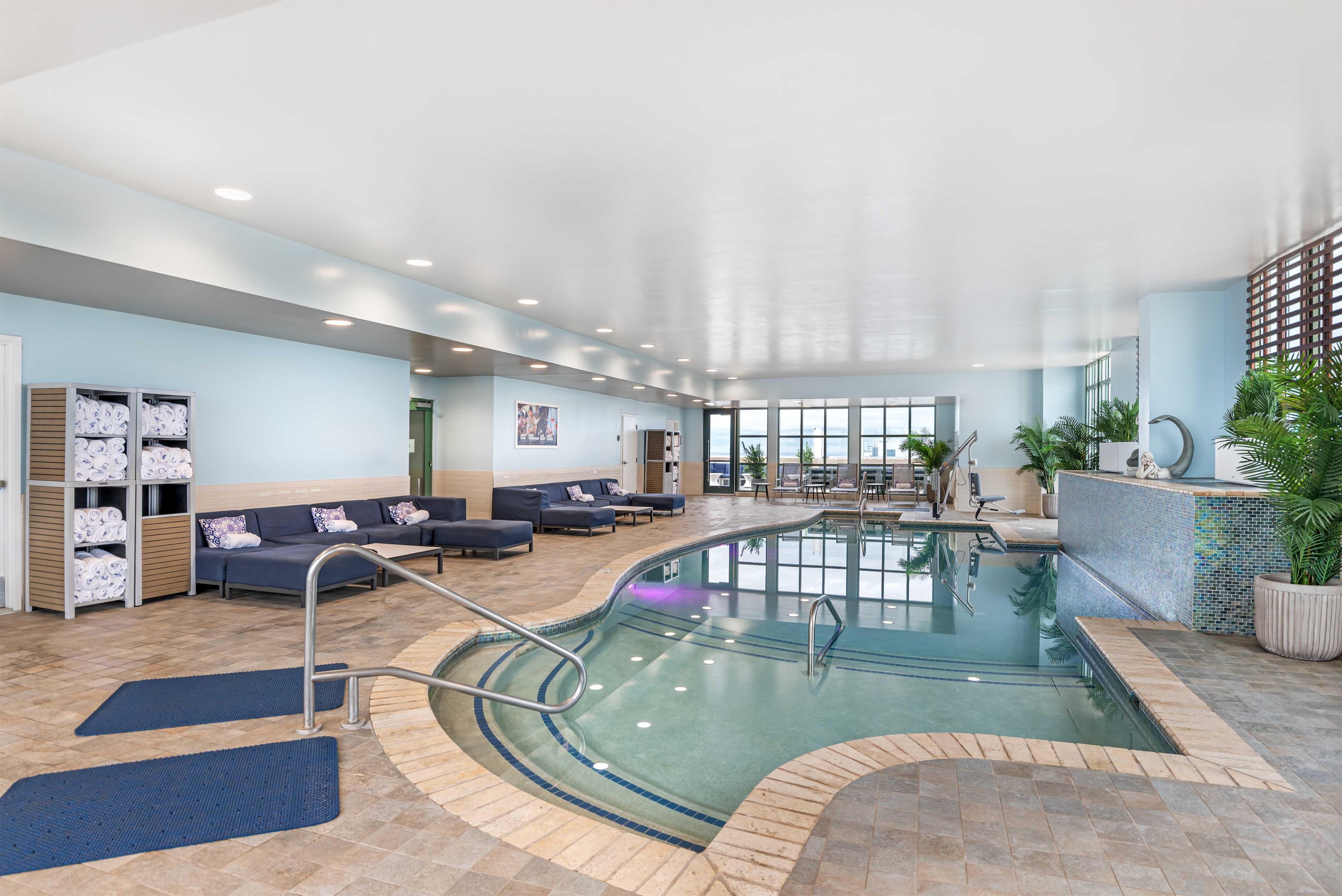 An indoor swimming pool with a lounge area, seating, and a view of the outdoors.