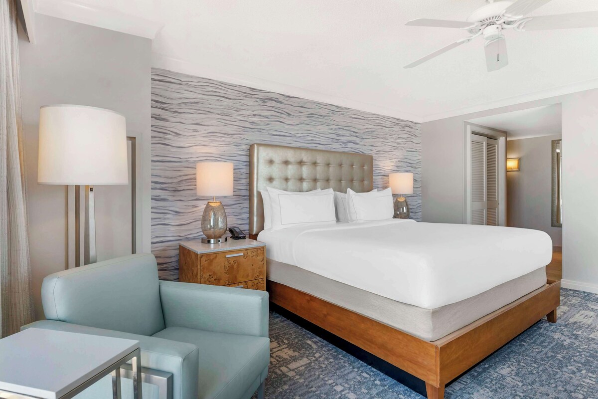 A hotel room with a large bed, two bedside lamps, a nightstand, a chair, and a ceiling fan.