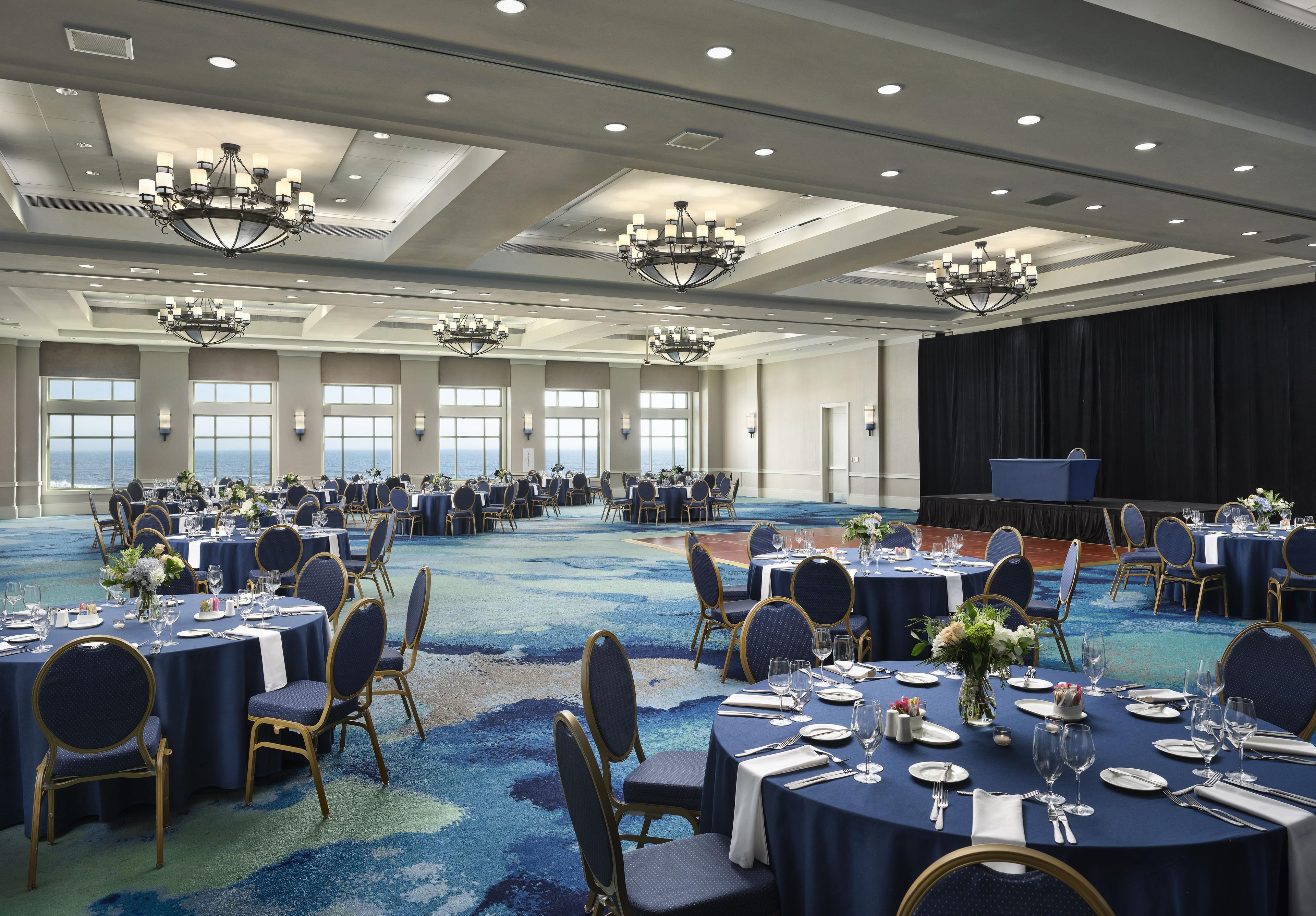 Une grande salle de banquet avec des tables rondes, des chaises et des lustres.