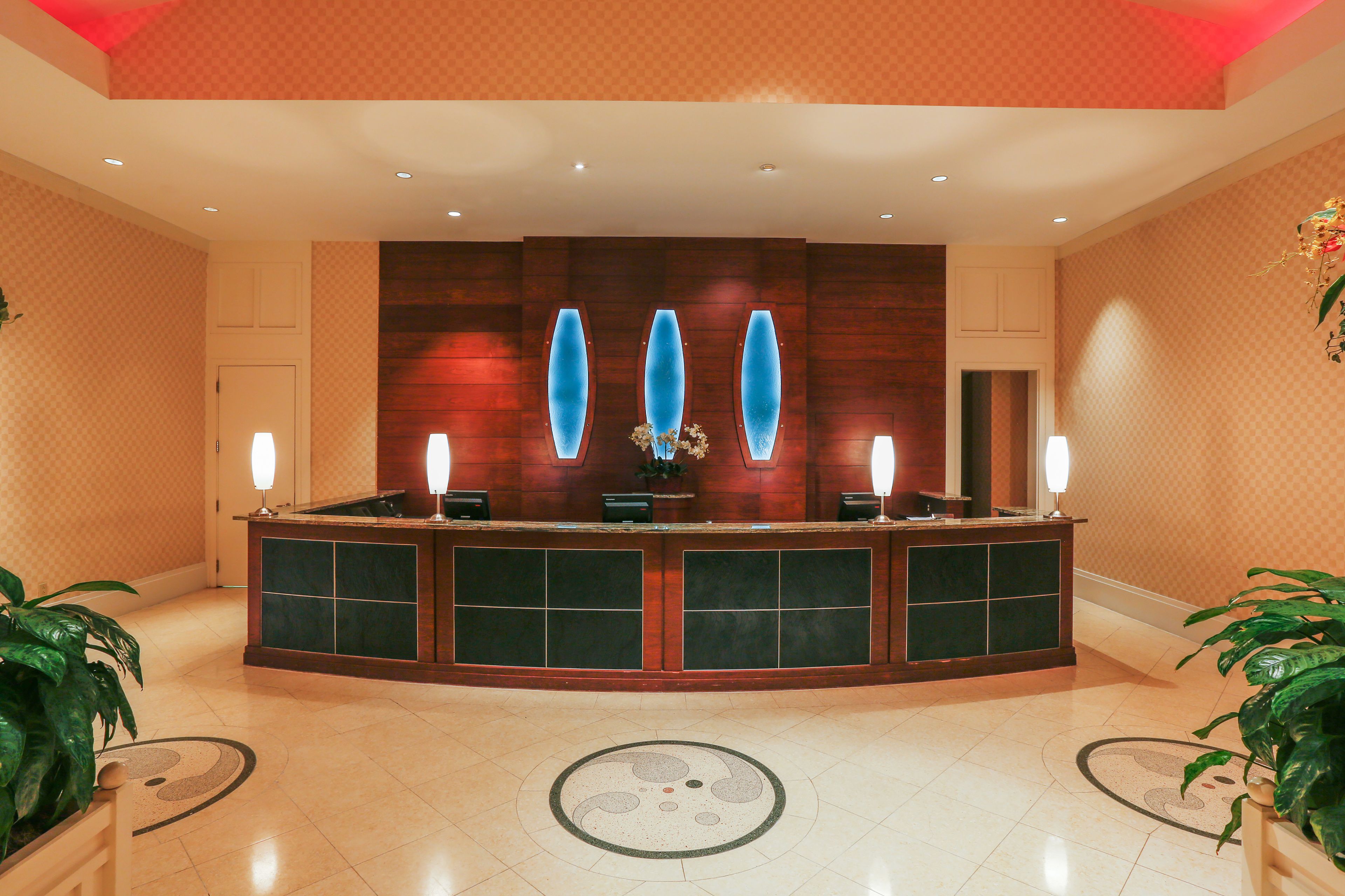 A reception area with a wooden reception desk, two lamps, and a decorative wall with three blue vases.