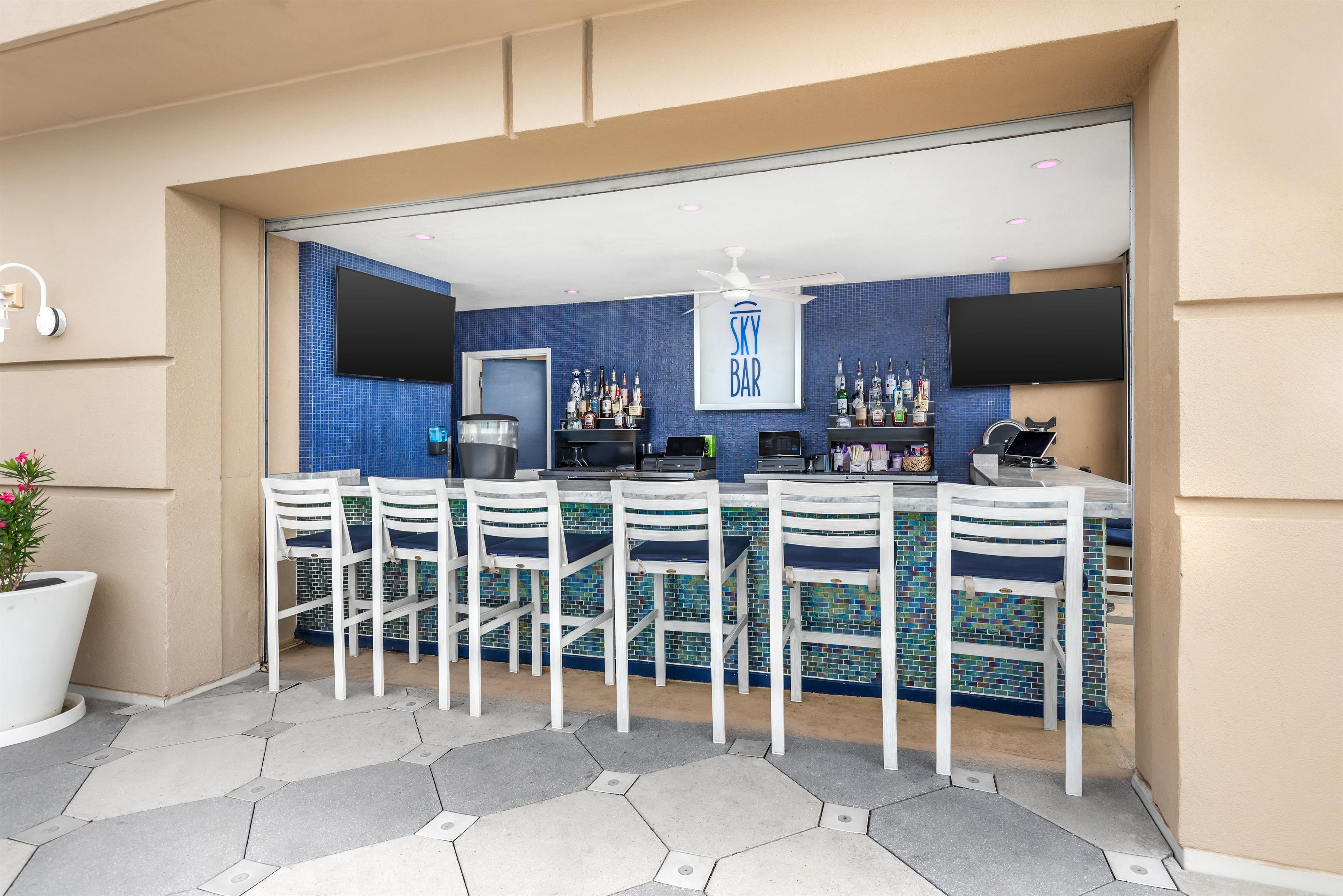 A bar area with a blue tiled backsplash, a 'SKY BAR' sign, and a row of white bar stools.