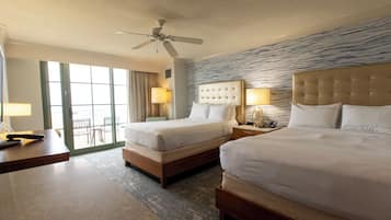Ein Hotelzimmer mit zwei Betten, einem Deckenventilator, einem großen Fenster mit Vorhängen und Blick ins Freie.