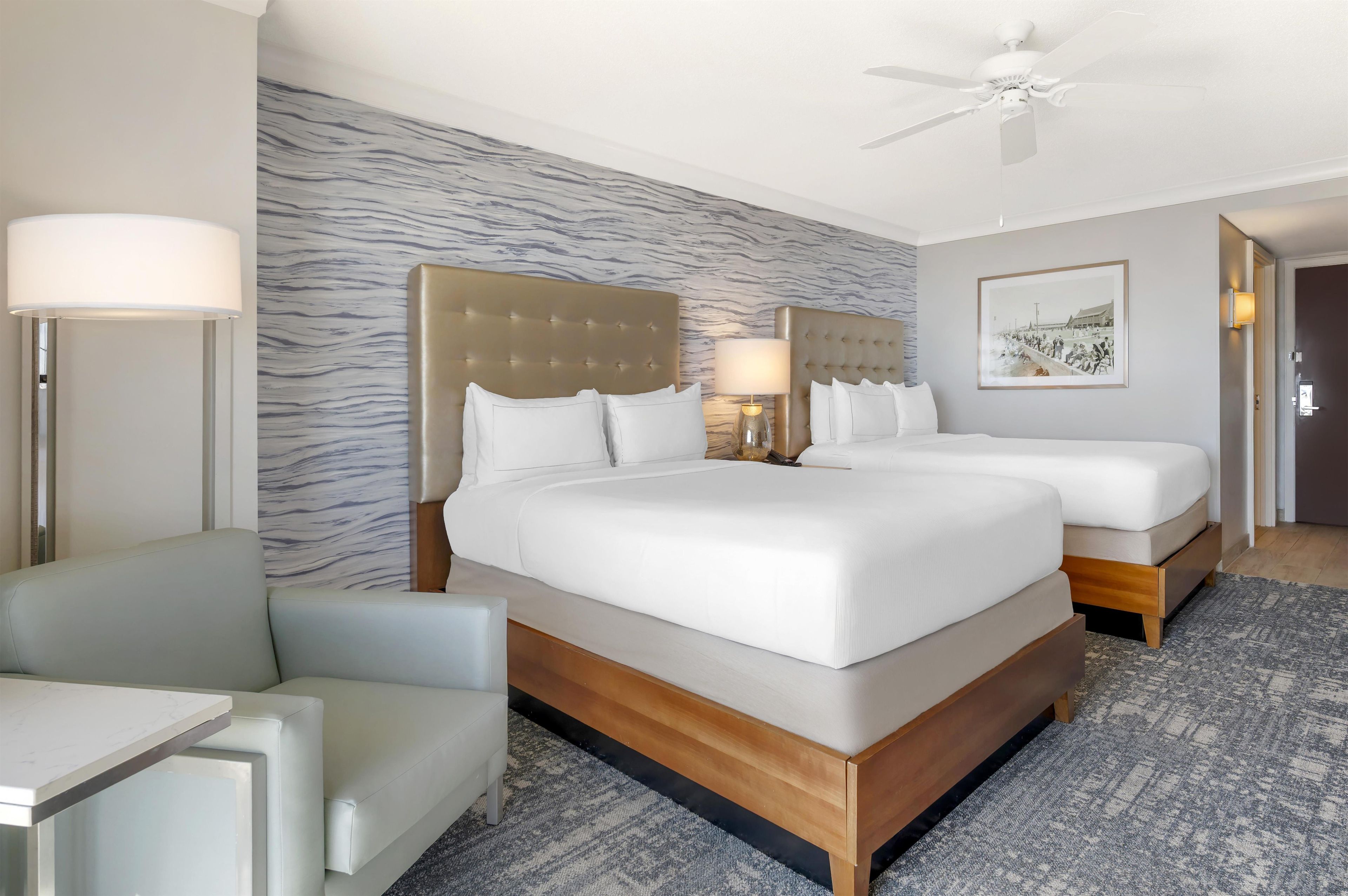 A hotel room with a large bed, two bedside tables, a chair, a ceiling fan, and a patterned wall.