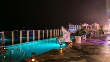 A nighttime swimming pool area with a clear view of the pool, a covered seating area, and a potted plant.