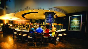 A bar area with round tables and chairs, a central pillar, and a menu board on the wall. - Hilton Virginia Beach Oceanfront (Virginia Beach)