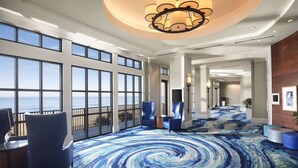 A spacious hotel lobby with large windows offering ocean views, a modern chandelier, and a blue patterned carpet. - Hilton Virginia Beach Oceanfront (Virginia Beach)