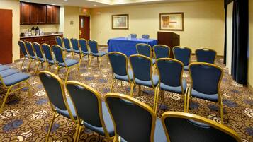A conference room with rows of chairs, a table, and a kitchenette area.