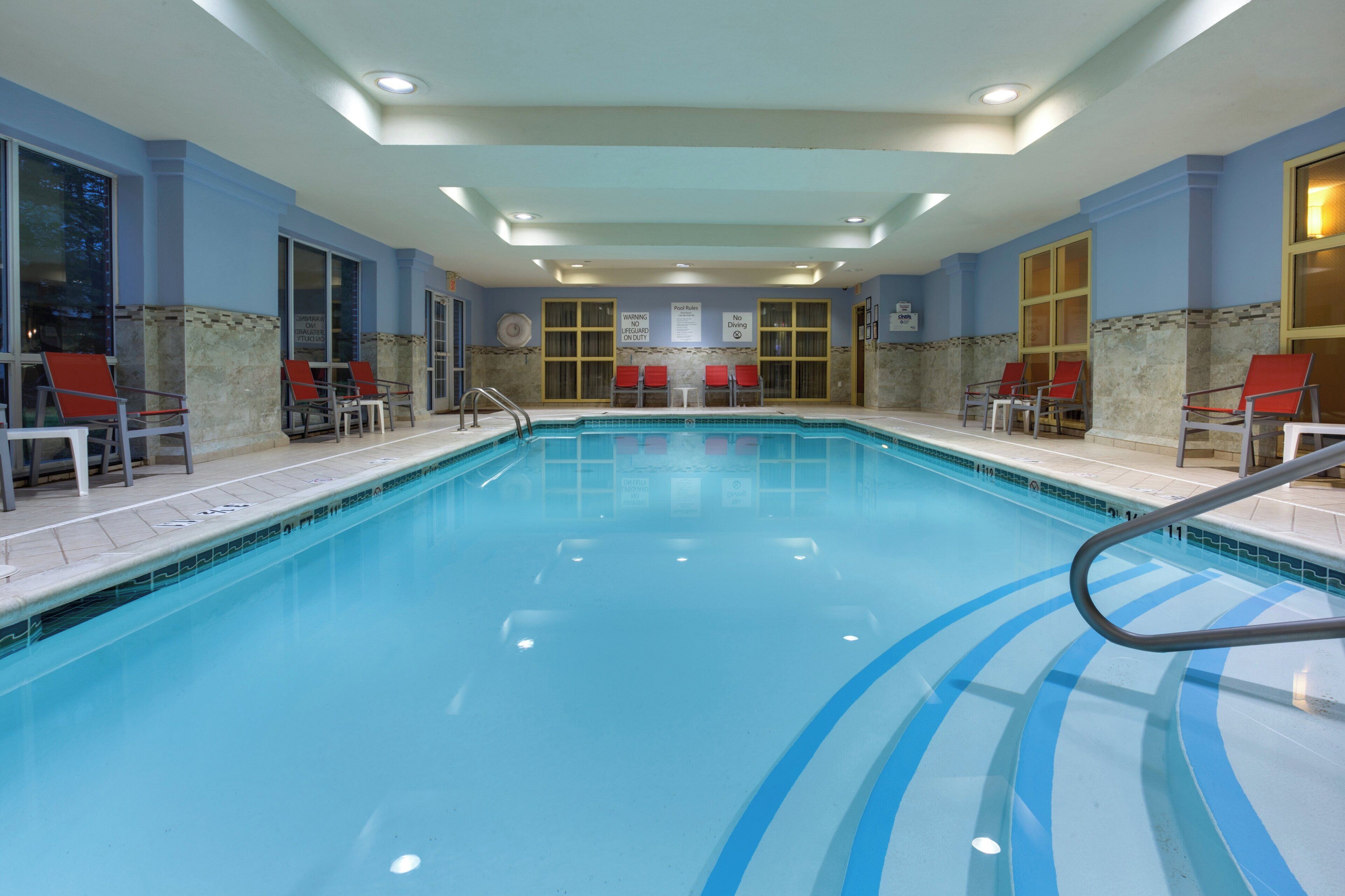 Une piscine intérieure à l’eau claire, entourée de chaises rouges et dotée d’un sol carrelé.