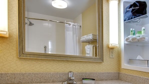 A bathroom with a large mirror, a sink, a shower, and a towel rack.
