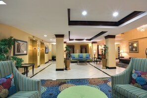 A hotel lobby with a central seating area, a reception desk, and a staircase leading to the upper floors. - Holiday Inn Express Tower Center by IHG (East Brunswick)