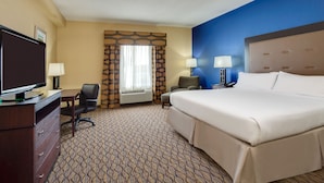 A hotel room with a large bed, a desk with a television, two chairs, and a window with curtains.