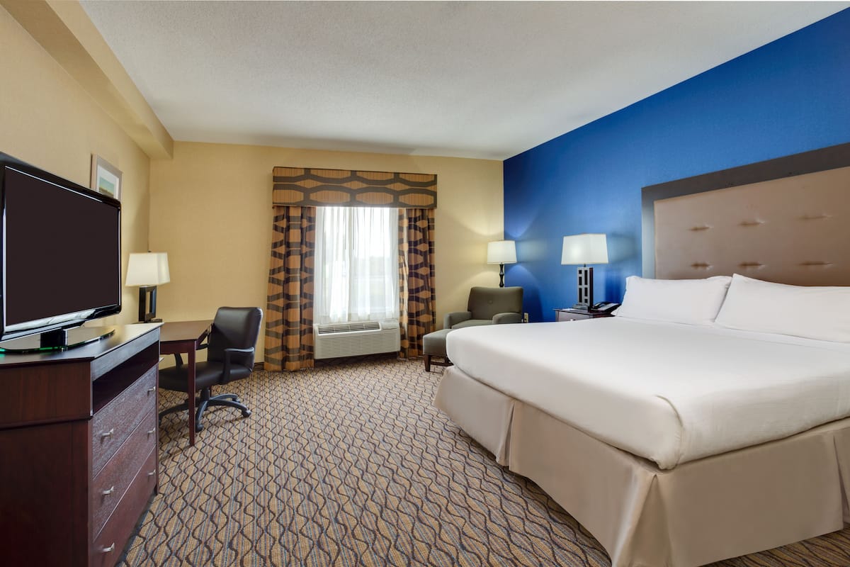 A hotel room with a large bed, a desk with a television, two chairs, and a window with curtains.