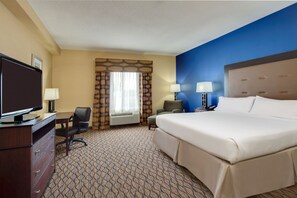 A hotel room with a large bed, a desk with a television, two chairs, and a window with curtains. - Holiday Inn Express Tower Center by IHG (East Brunswick)