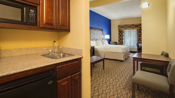 A hotel room with a kitchenette, a bed, a desk, and a chair.