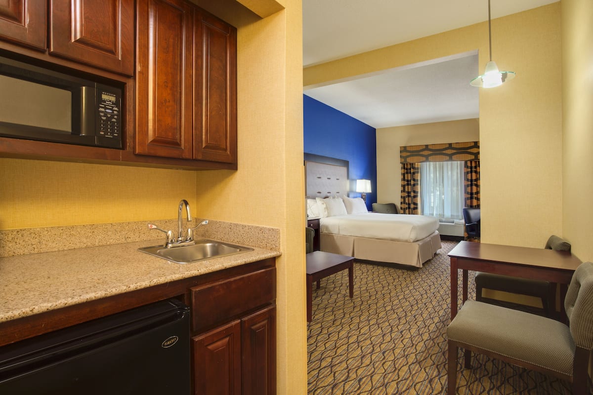 A hotel room with a kitchenette, a bed, a desk, and a chair.