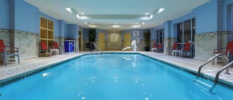 A large indoor swimming pool with clear blue water, surrounded by lounge chairs and a pool lift.
