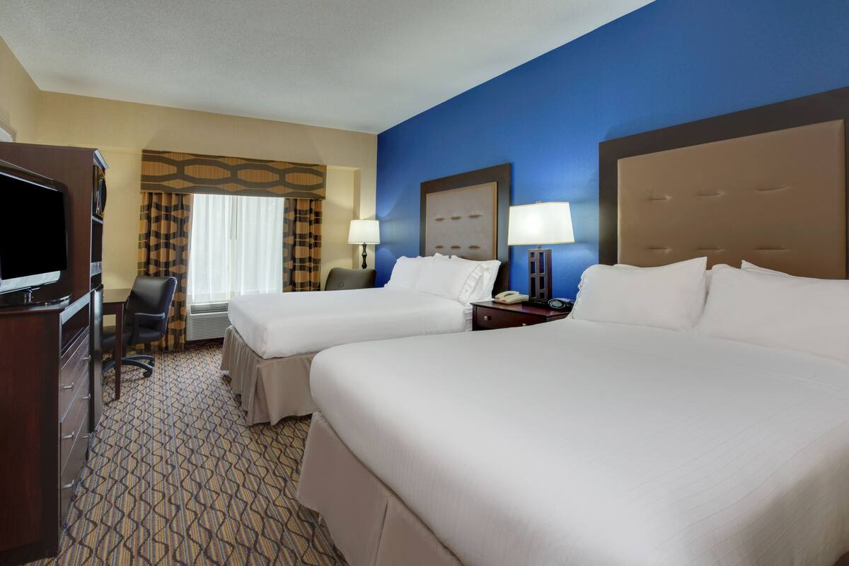 A hotel room with two beds, a desk, a chair, a TV, and a window with curtains.
