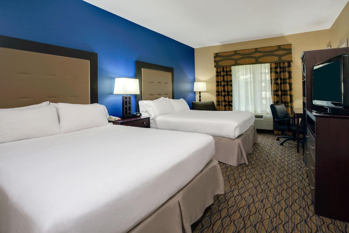 A hotel room with two beds, a desk with a chair, a television, and a desk lamp.