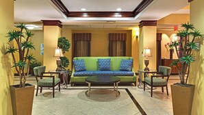 A hotel lobby with a green sofa, two armchairs, a coffee table, and potted plants. - Holiday Inn Express Tower Center by IHG (East Brunswick)