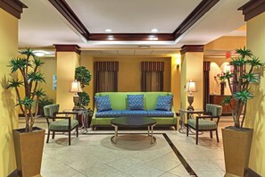 A hotel lobby with a green sofa, two armchairs, a coffee table, and potted plants. - Holiday Inn Express Tower Center by IHG (East Brunswick)