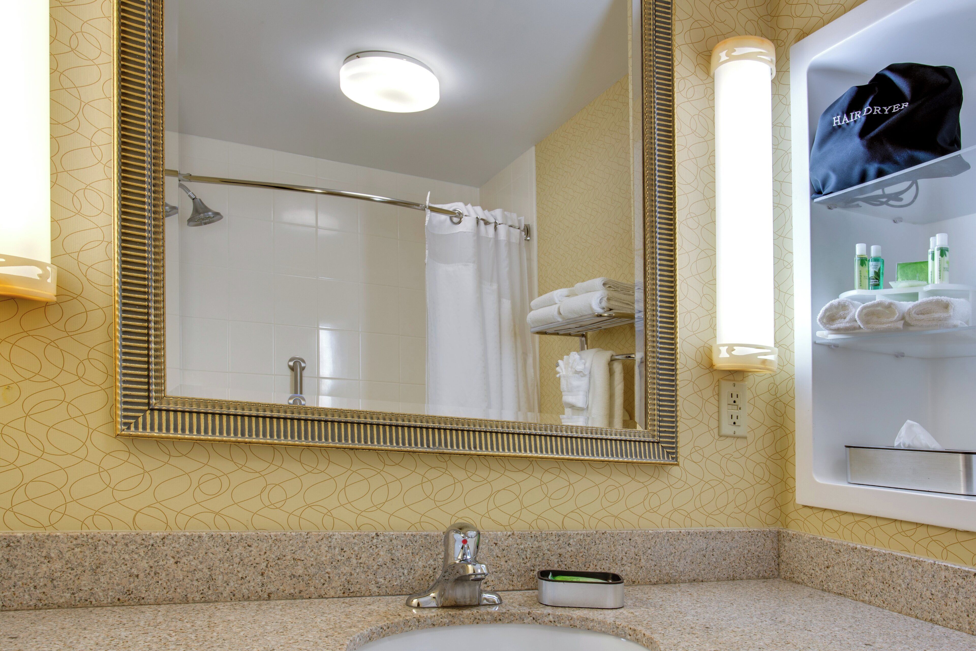 A bathroom with a large mirror, a shower, a sink, and a towel rack.