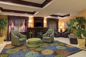 A living room with a fireplace, two armchairs, a sofa, and a patterned rug. - Holiday Inn Express Tower Center by IHG (East Brunswick)