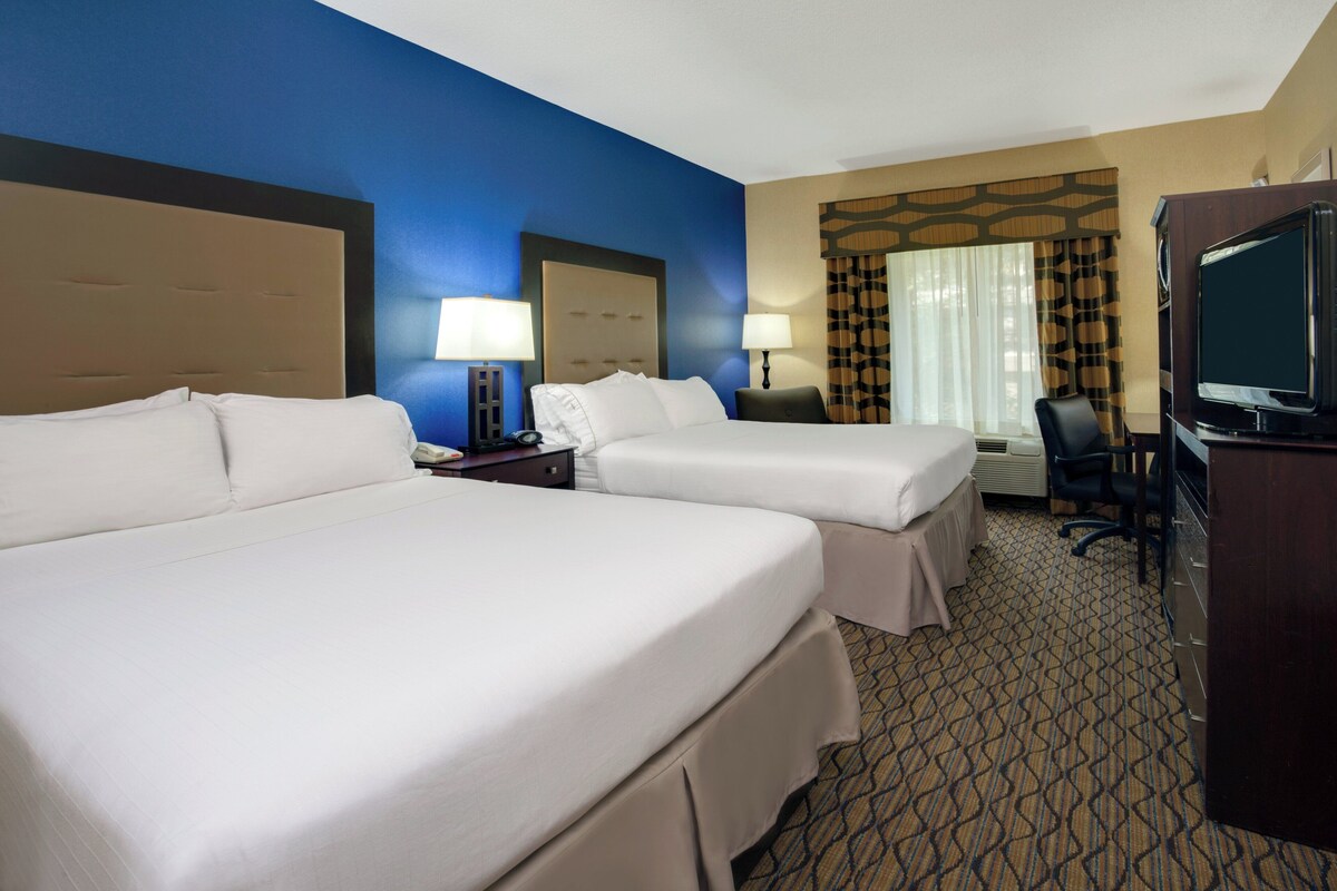 A hotel room with two beds, a desk, a television, and a window with curtains.
